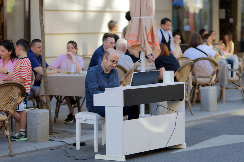 10 - A man in a patterned blue button-down shirt playing a digital piano on a cafe terrace